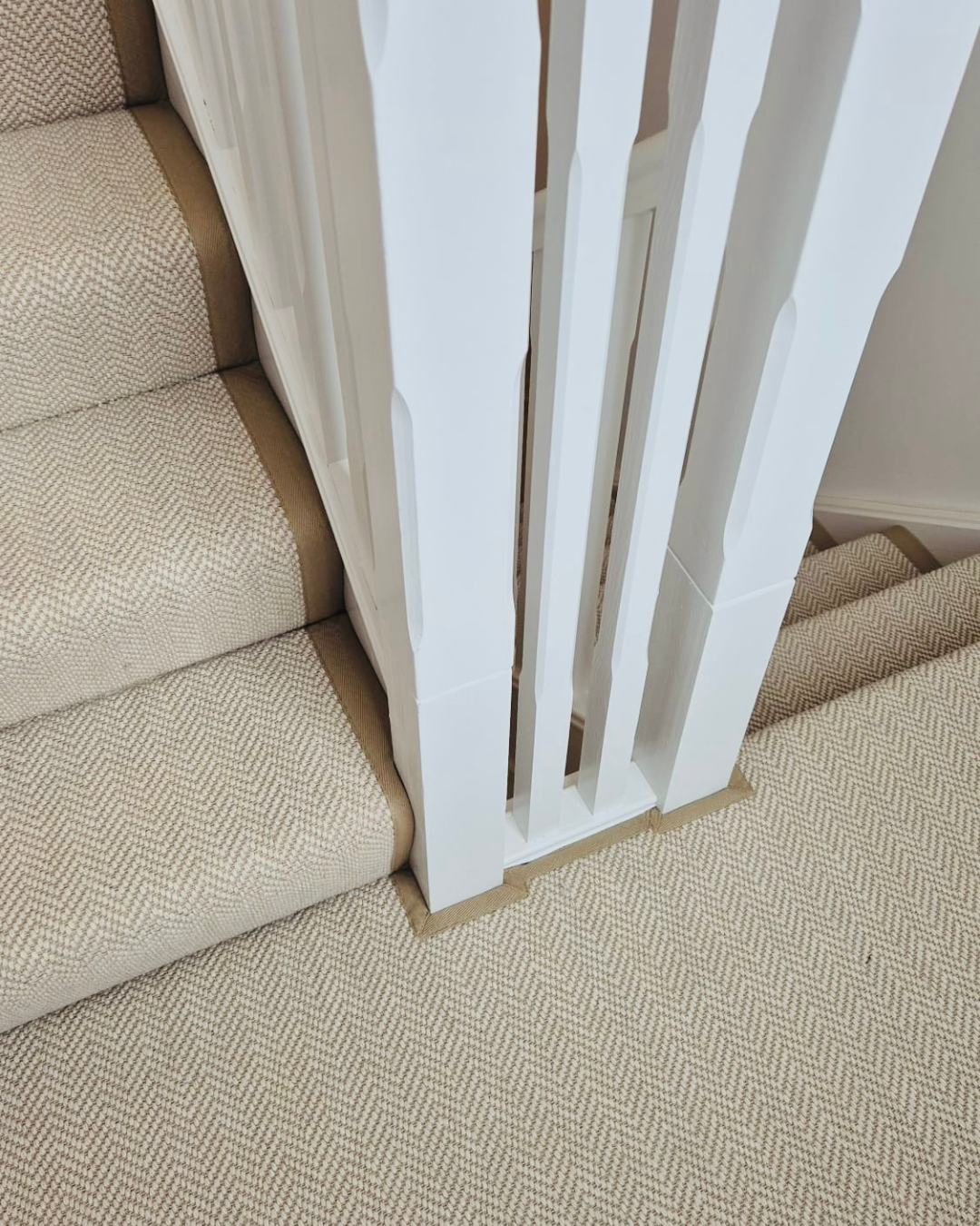 Neutral stair runner with a taupe border neatly fitted around white landing balustrades