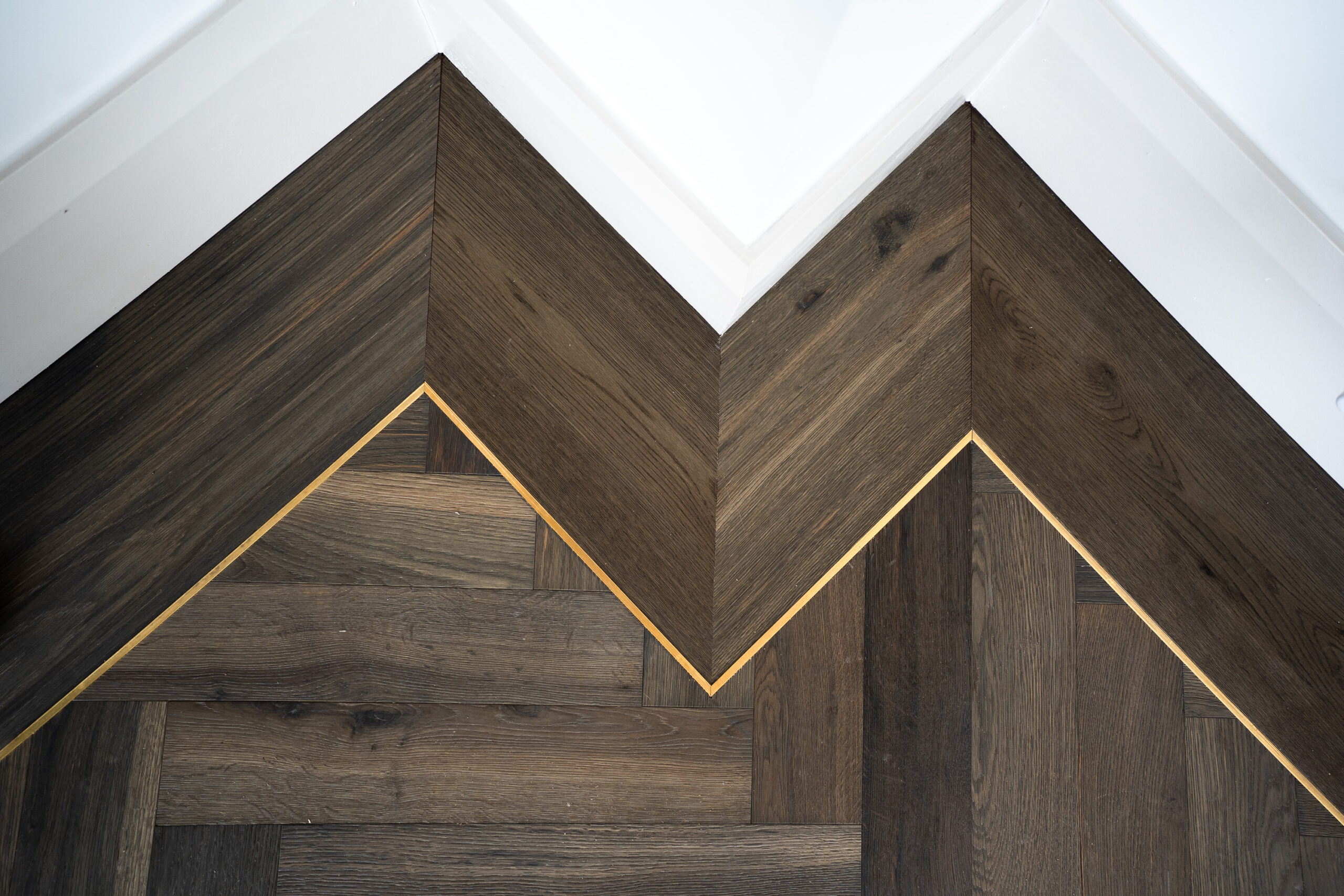 Engineered walnut herringbone flooring with a gold inlay and mitred border