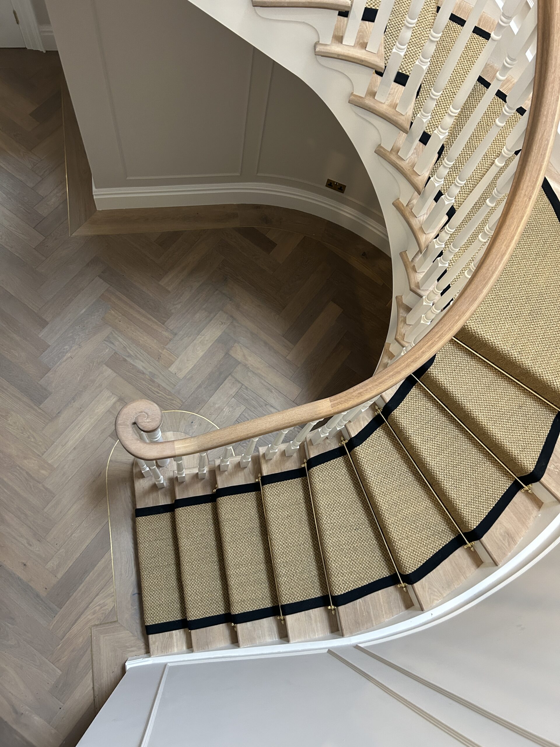 Overhead view of the curved staircase, black bordered runner and brass inlay in the herringbone floor