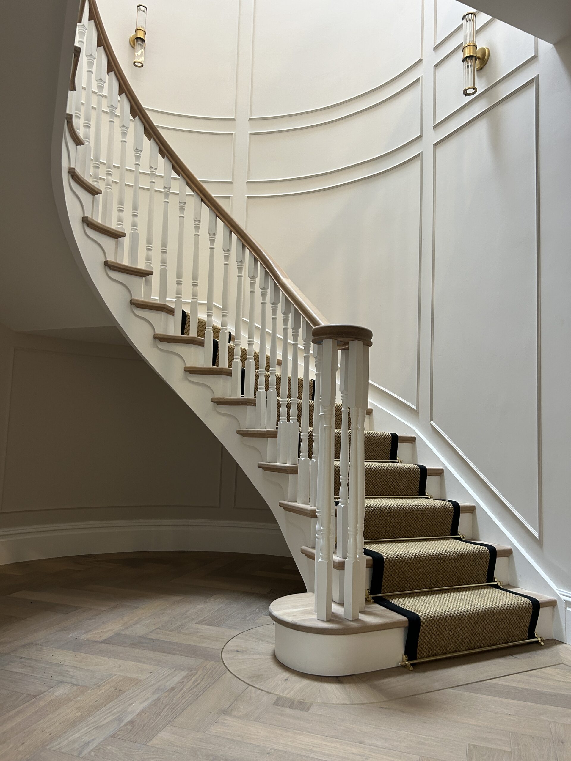 Bespoke neutral stair runner with black trim and brass rods on a sweeping timber staircase