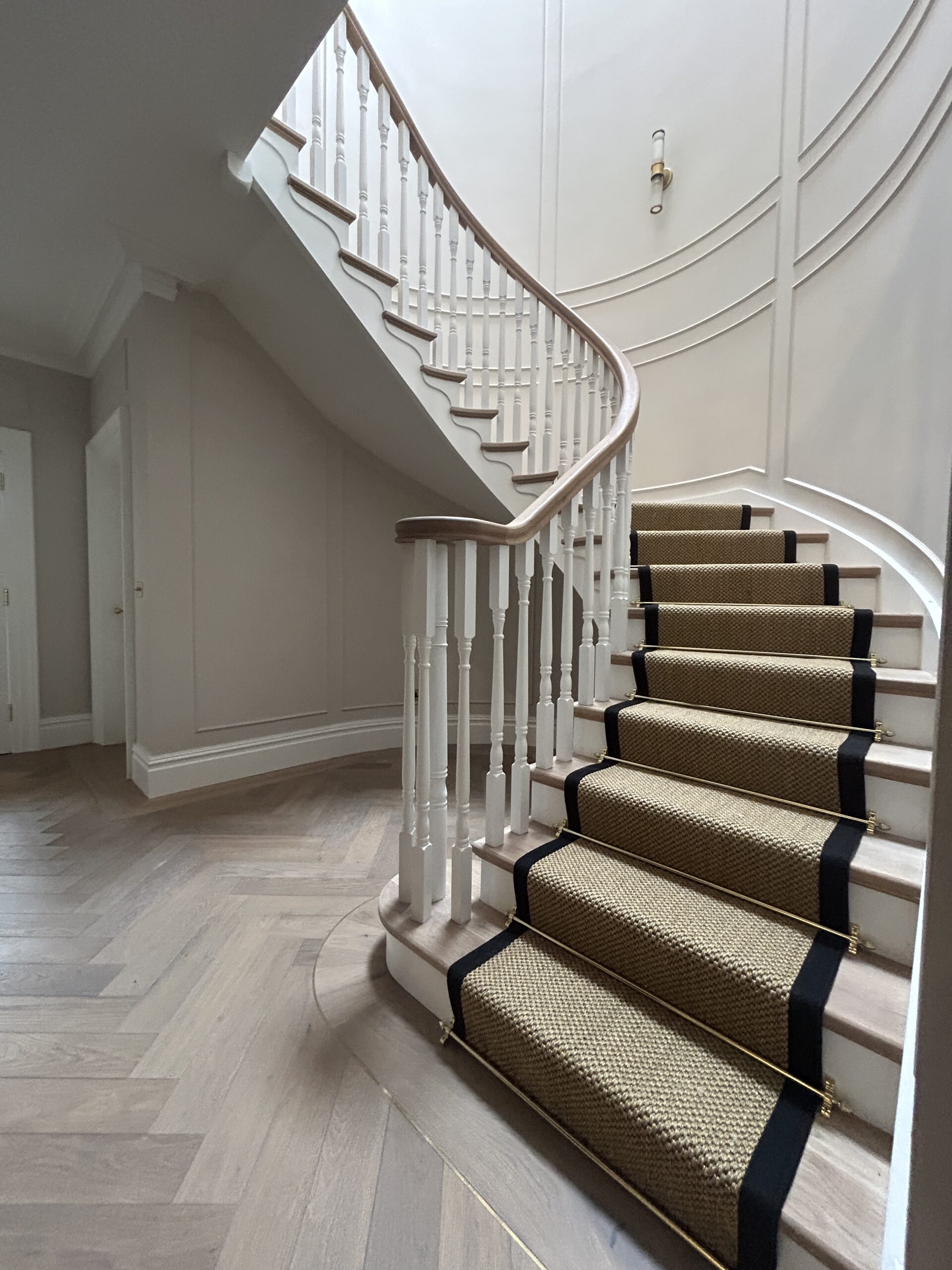 Warm textured stair runner edged in black and finished with elegant brass stair rods